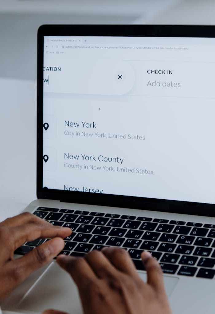 Hands typing on a laptop near New York location search screen.